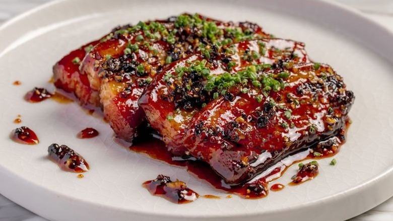 Thick slices of glazed bacon sprinkled with chopped chives on a white plate at High Steaks Vegas