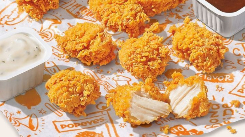 Popeyes chicken nuggets are scattered across a table next to dipping sauces