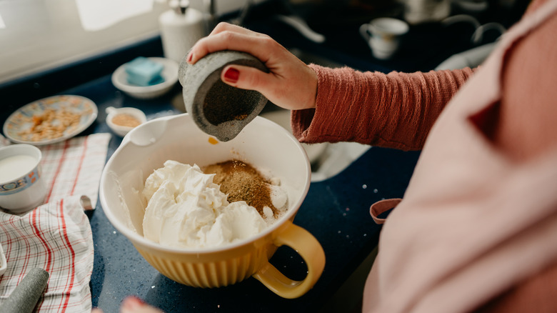 Chef dumping spices into a bowl of whipped filling