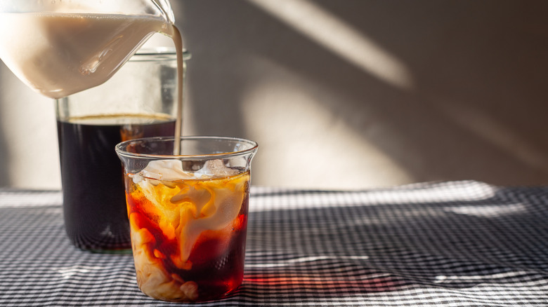 Milk is poured into a glass of iced coffee