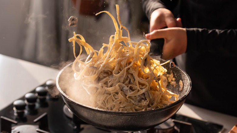 Chef tossing pasta and sauce over stove