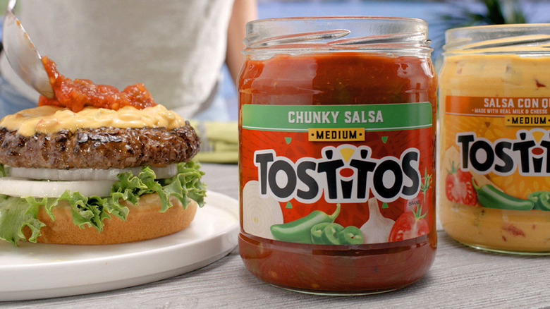 Jars of salsa and queso sit next to a hamburger.