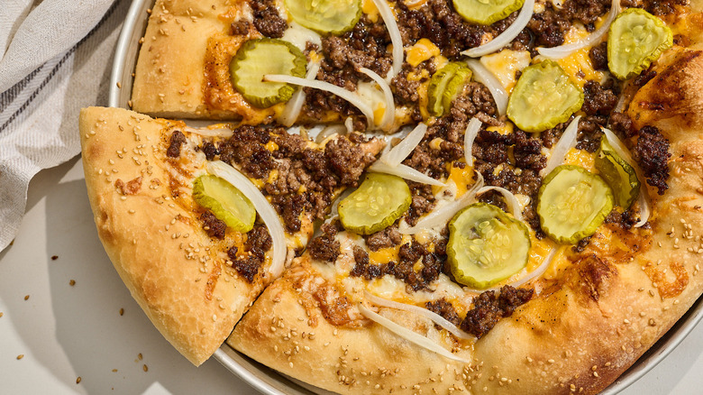 Slice of cheeseburger pizza pulled from full pizza