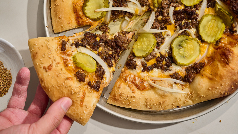 Hand pulling slice from full pizza