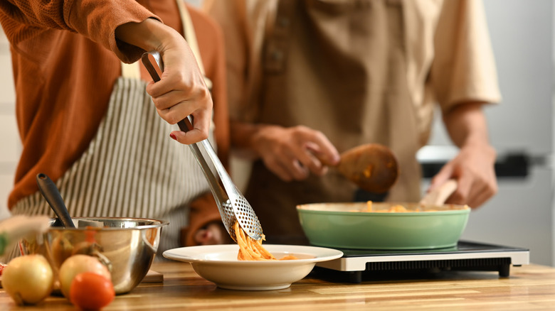 A couple cooking pasta together in the kitchen.