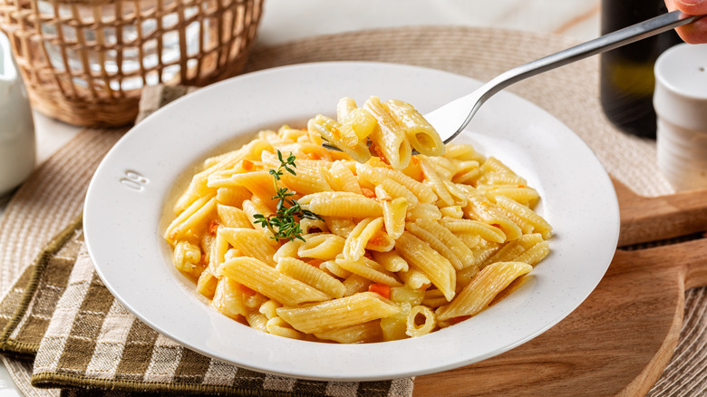 A bowl of creamy pasta with a sprig of thyme.