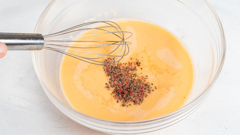 Bowl with beaten eggs, black pepper, and a whisk
