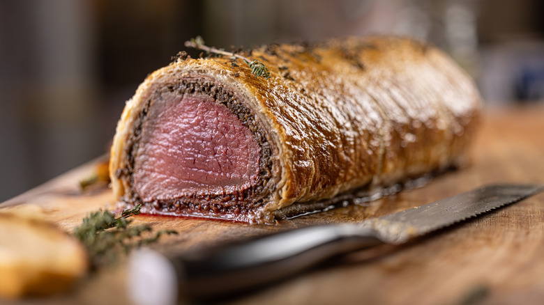 A beef Wellington cross-section on a wooden cutting board