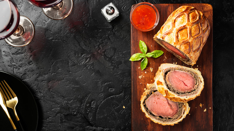 Birds-eye view of a beef Wellington next to a salt shaker and two glasses of red wine