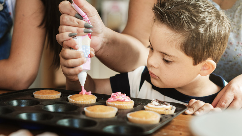 A family, including a small child, work together to decorate cupcakes