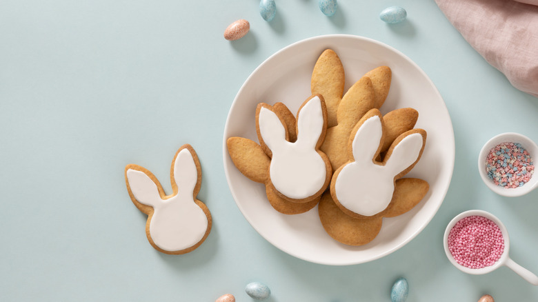Bunny-shaped cookies with white royal icing sit on a plate, ready to be decorated with sprinkles