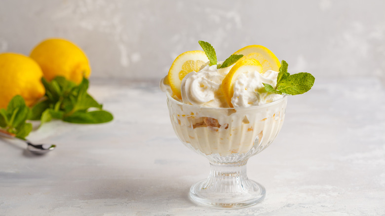 Lemon parfait with layered cake and cream with lemon slices and mint springs in a fancy glass cup