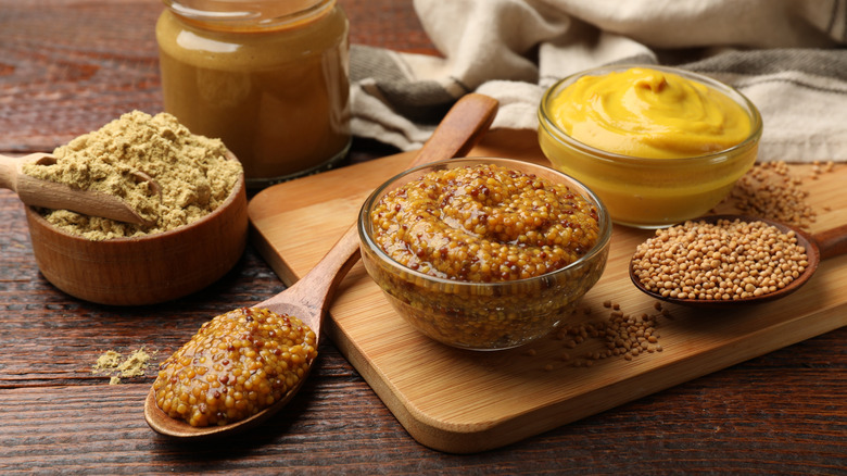 Different types of mustard on a wooden board