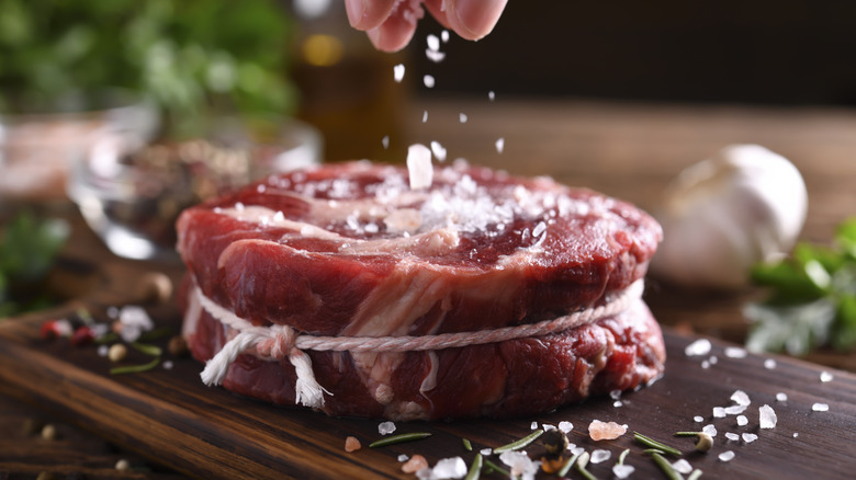 Chef sprinkling large grain salt on raw red meat.