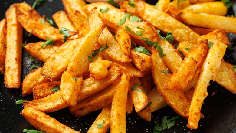 Seasoned fries garnished with herbs on a dark plate