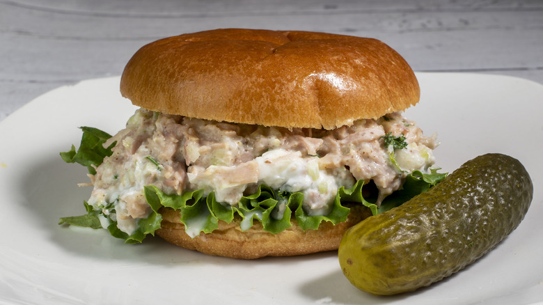 Chicken salad on brioche roll alongside a gherkin pickle