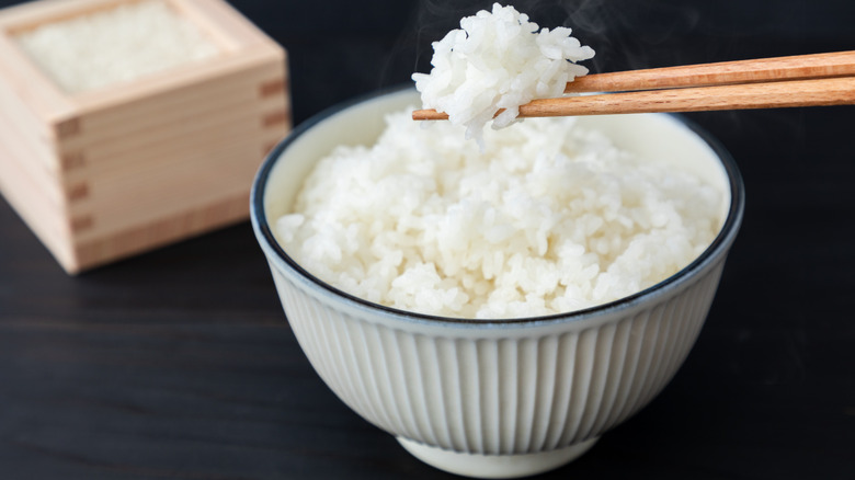 a bowl of steaming white rice with chopsticks