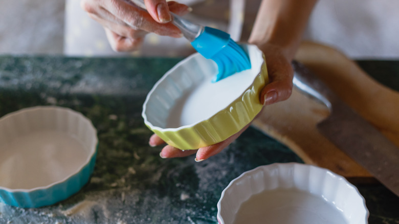 A woman uses a silicone brush to grease a pie plate