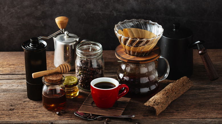 A pour-over coffee setup with a coffee grinder, honey, and a red cup of black coffee