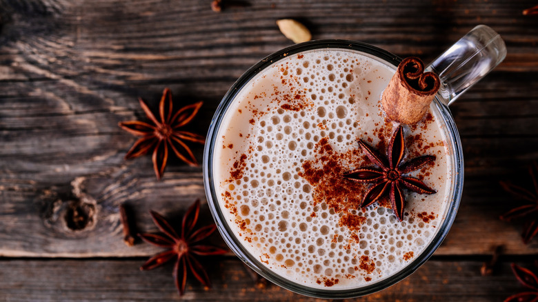 A chai latte in a glass mug has star anise and a cinnamon stick as garnishes