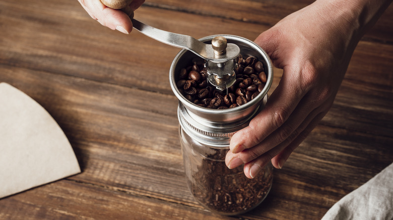 A person holds a manual coffee grinder while grinding coffee beans