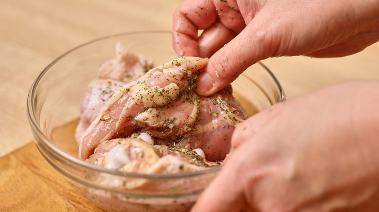 Someone puts raw chicken into a marinade.