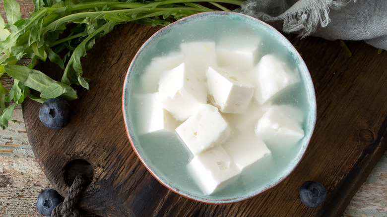 A bowl of feta cheese in brine on a wooden board.