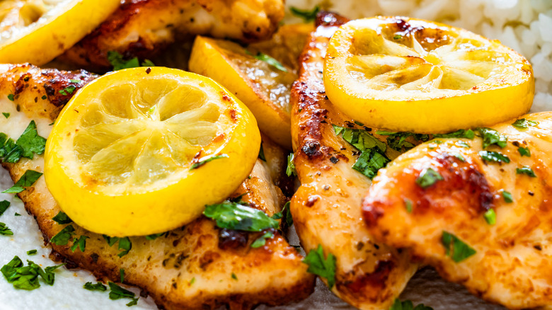 A plate of grilled chicken covered with lemons.