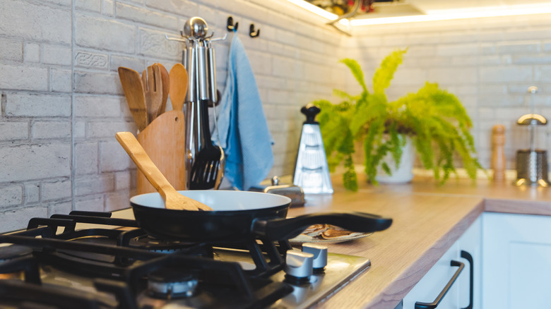 Frying pan on stovetop with utensils in canister nearby