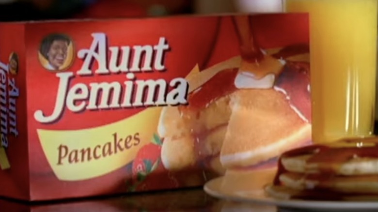 Aunt Jemima box behind a plate of syrup smothered pancakes with a glass of orange juice