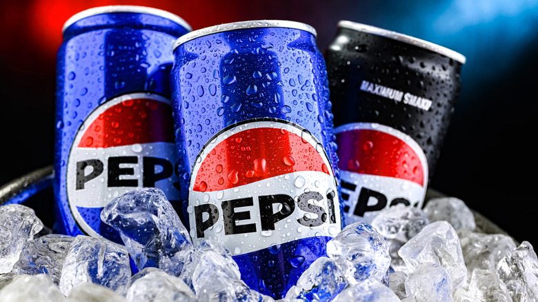 Condensation collects on three cans of Pepsi jutting out of a pile of ice cubes