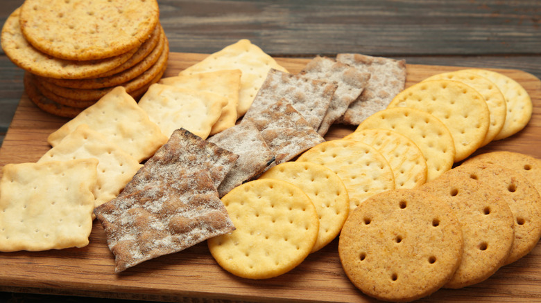 A variety of different crackers on a wooden serving board.