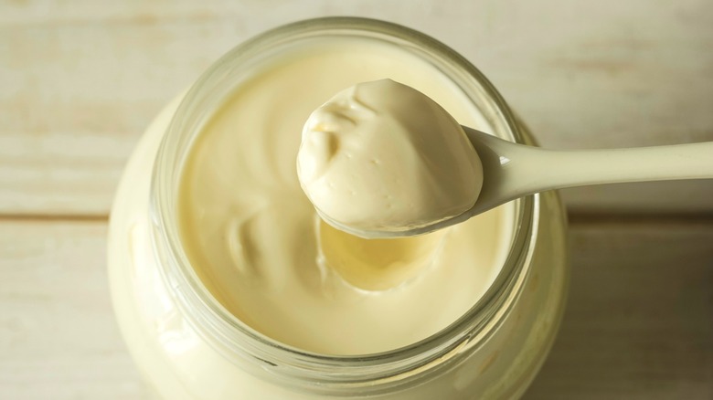 jar of mayonnaise with a spoon full of mayo on a wooden table