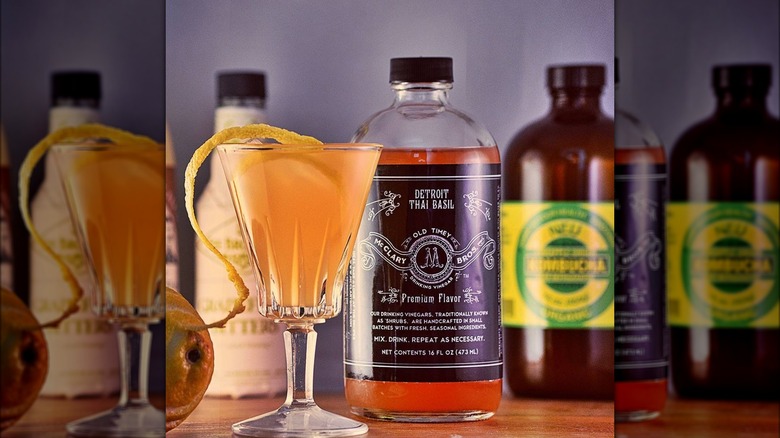 A cocktail in a glass with bottle of McClary Bros drinking vinegar