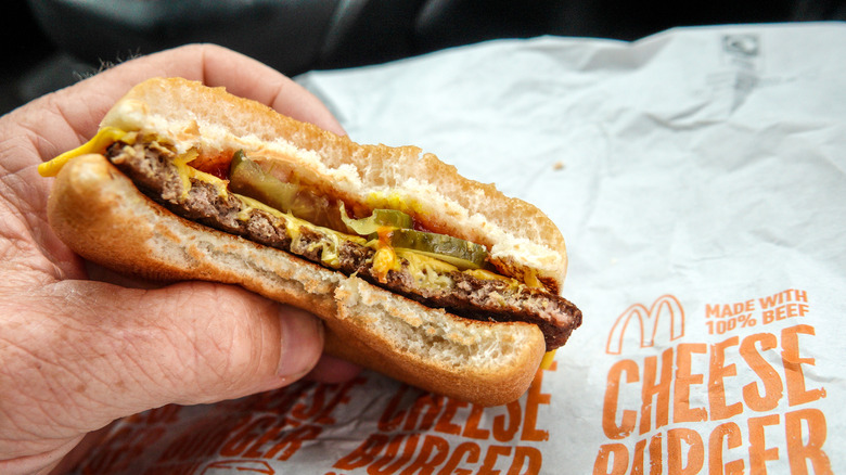 Someone holds a half-eaten McDonald's cheeseburger.