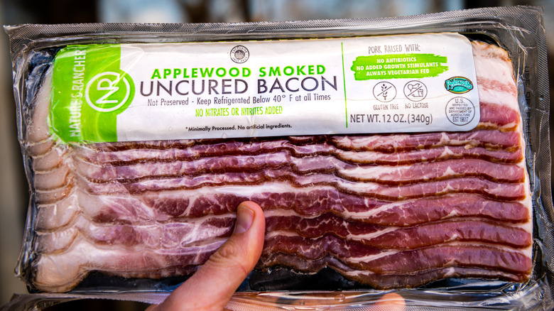 Hand holding a pack of applewood smoked bacon