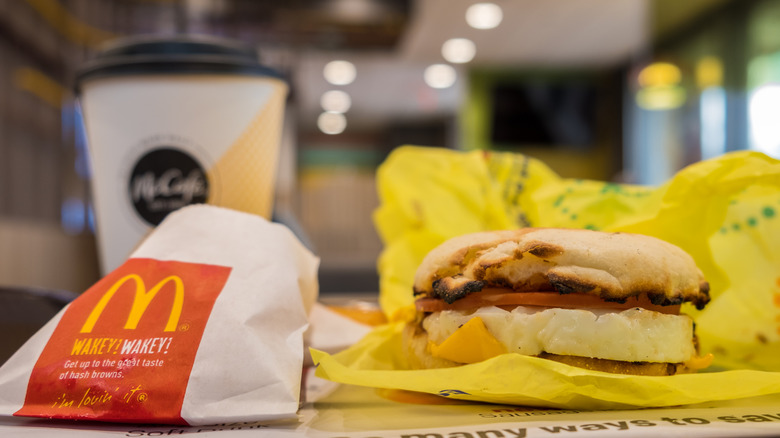 An Egg McMuffin sits on its unfolded wrapper next to a cup of McDonald's coffee and some hashbrowns.