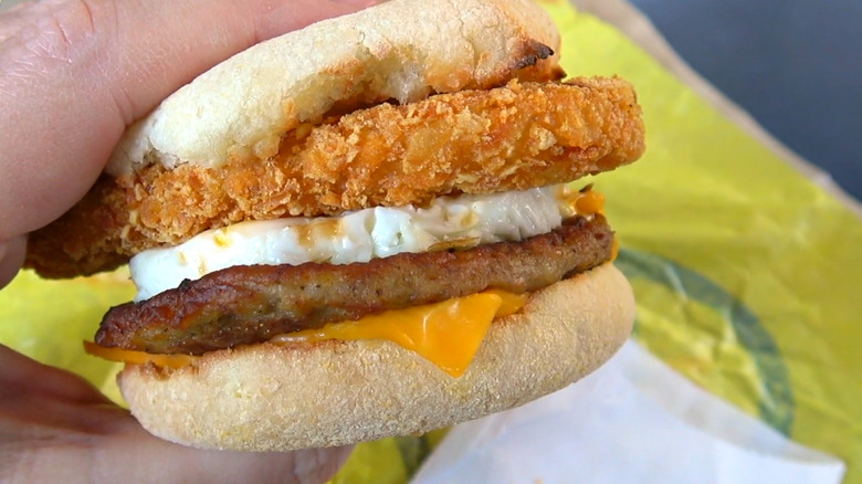 Someone holds a Sausage McMuffin with an added hash brown.