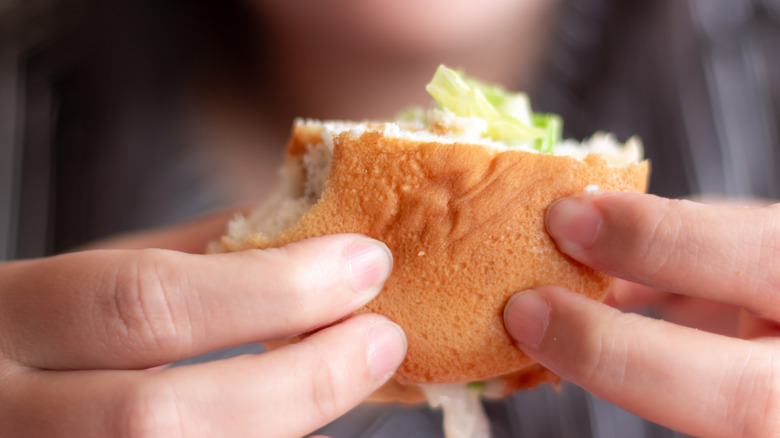 Hands hold up a partially eaten fish sandwich
