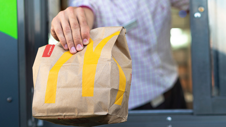 A hand holds a McDonald's food bag through a takeout window.