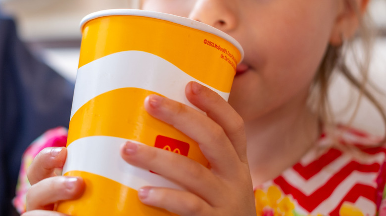 A young girl drinks from a McDonald's soda cup
