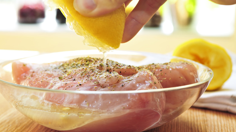 person squeezing lemon over raw seasoned chicken