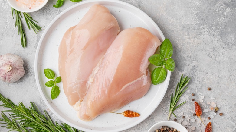 raw chicken breasts on white plate with herbs