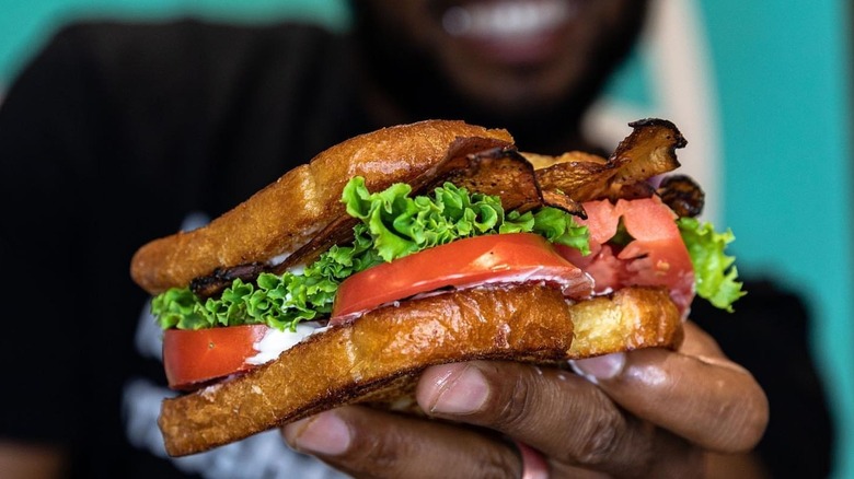 Someone holds out a BLT made with mushroom bacon