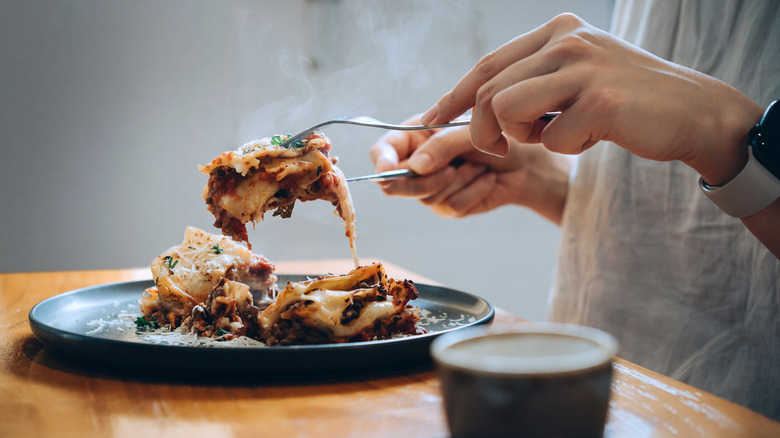 A person picking up a piece of lasagna from their plate