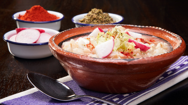 A bowl of pozole next to radishes and spices