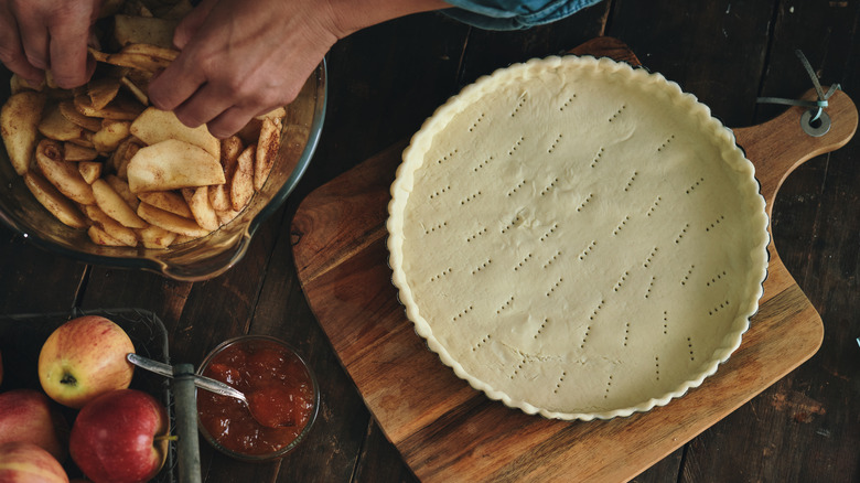 prepared pie crust in pan with bowl of apple pie filling