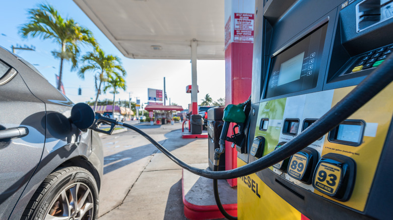 A car at a gas pump filling up on gas with palm trees in the background.