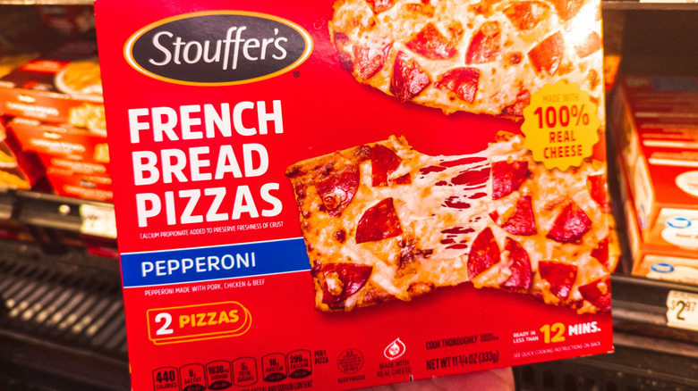 A hand holds a box of Stouffer's French Bread Pizza at the grocery store.