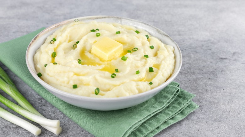 Scallions sit next to a white bowl filled with mashed potatoes